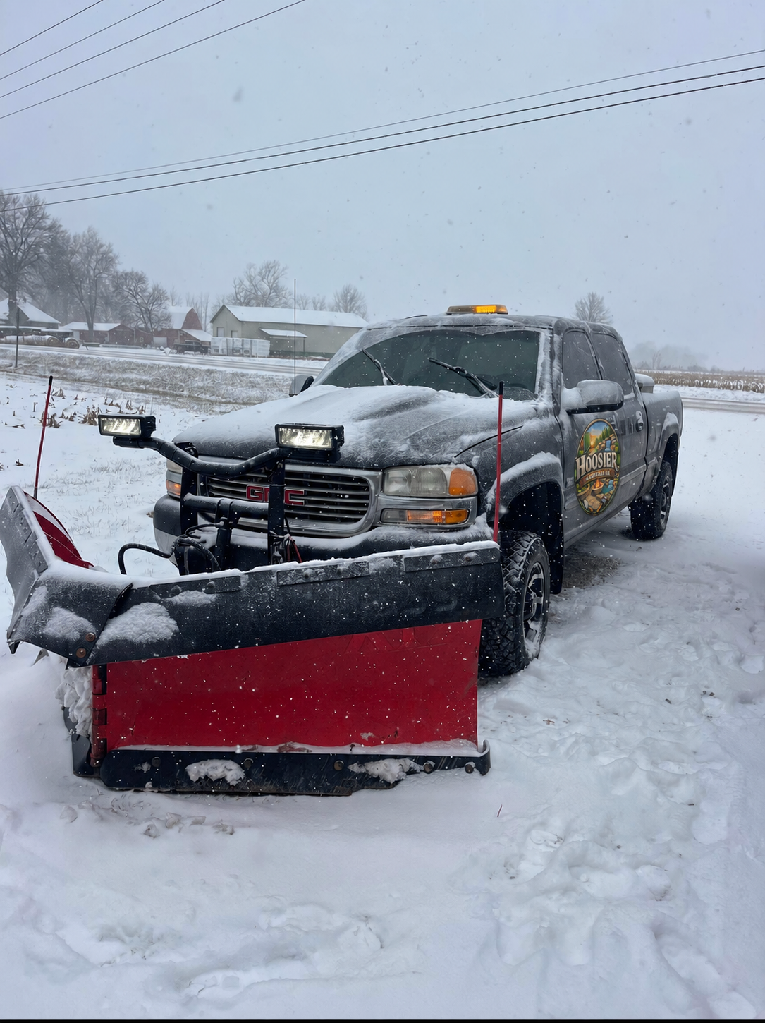 Toby’s GMC truck and red snowplow in the snow, with Hoosier Hardscape LLC branding on the door